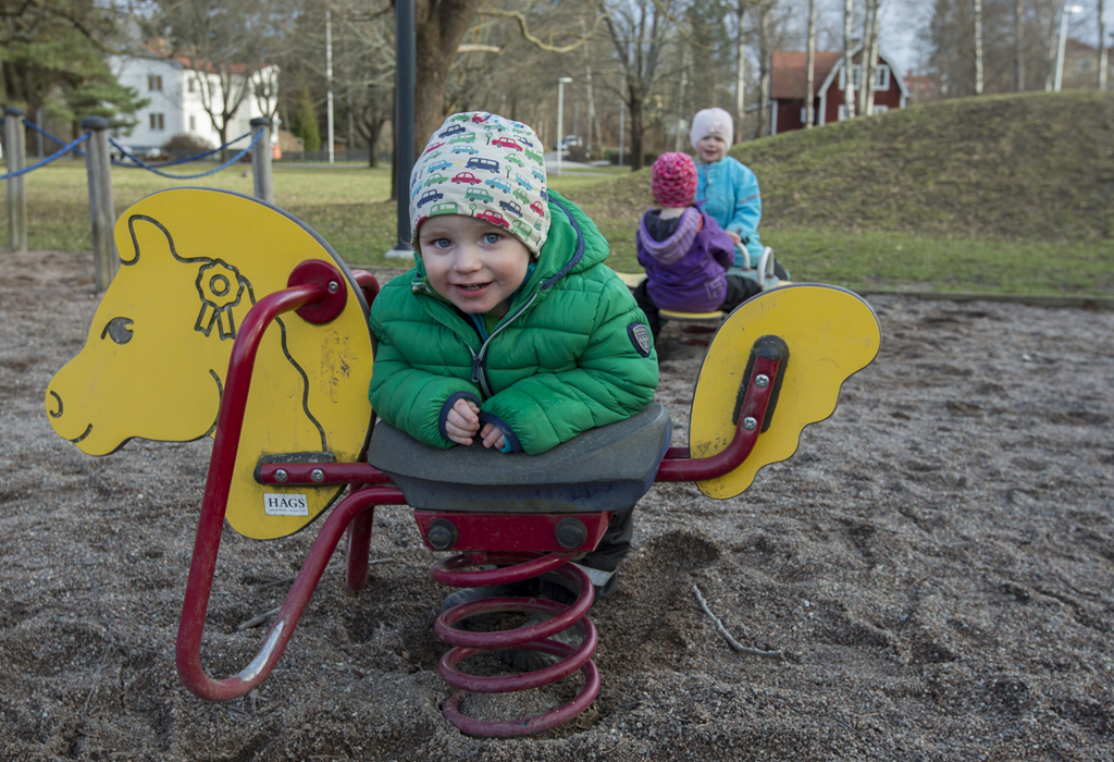 Barn rider på gunghästar i lekpark.