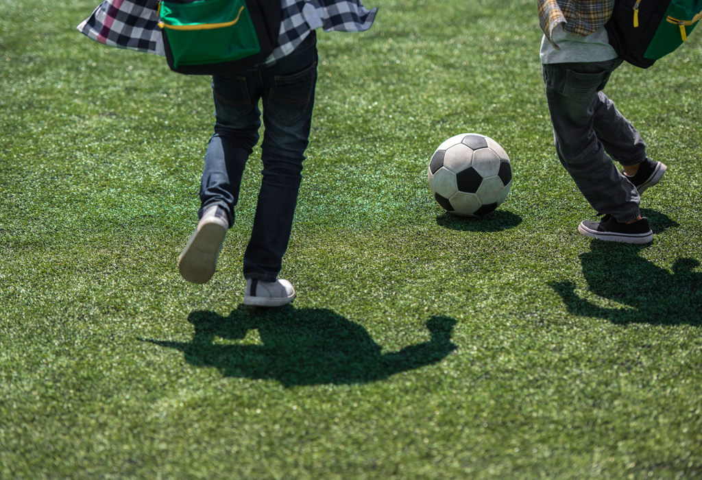 Två barn spelar fotboll på gräsmatta.