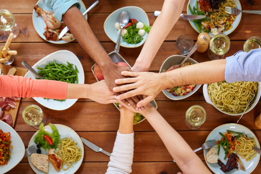 Händer som läggs på varandra över ett bord med olika maträtter.