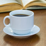 Kopp med kaffe, bok i bakgrunden.