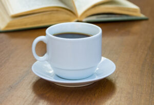 Kopp med kaffe, bok i bakgrunden.
