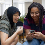 Two happy women looking in a mobil och smiles.