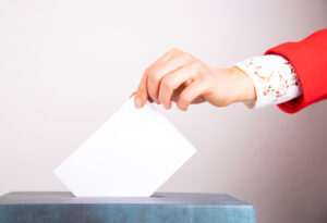 En kvinnas hand lägger en röst i låda under val.