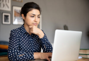 Kvinna sitter vid dator och skriver betänksamt.