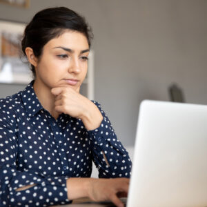 Kvinna sitter vid dator och skriver betänksamt.