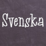 Svart tavla med texten Svenska skriven med vit krita.
