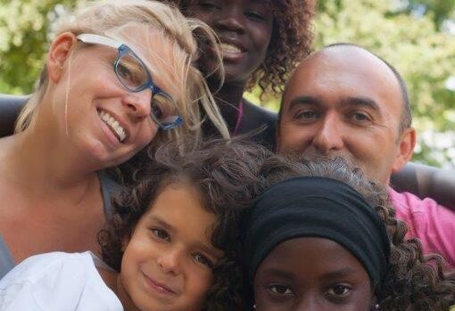 Etnisk familj med två vuxna och tre barn. Alla glada och med olika hudfärger.