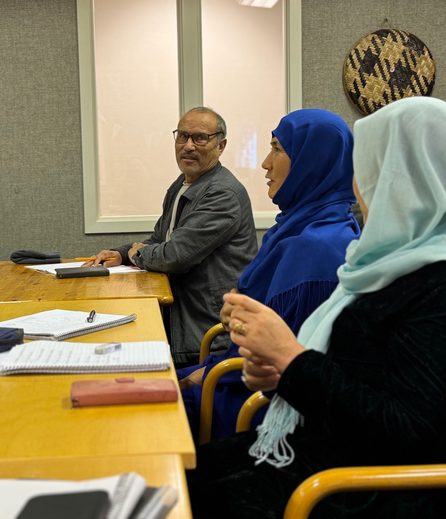 Tre deltagare, en man och två kvinnor sitter vid ett bord med block och pennor framför sig.