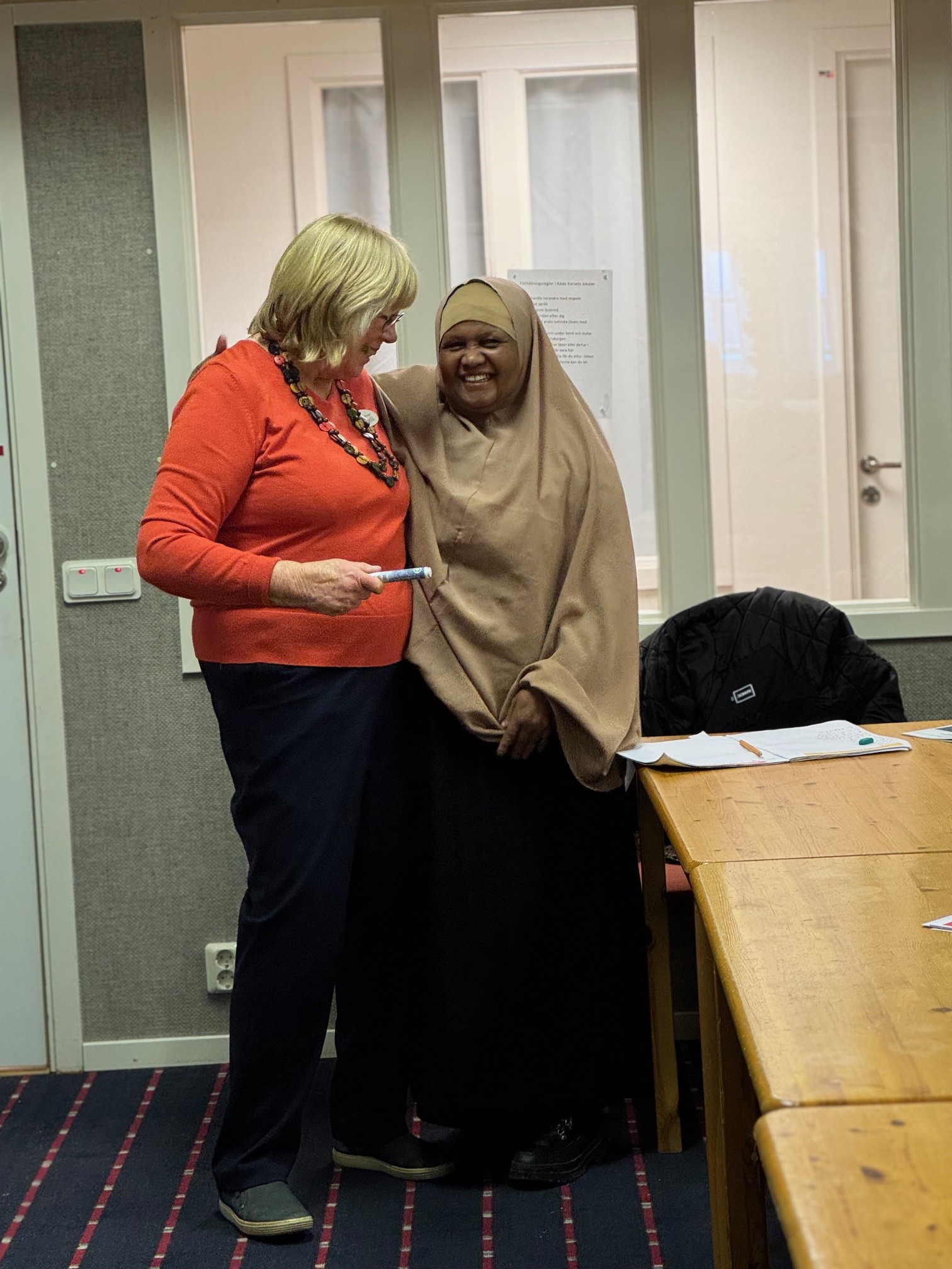 Den kvinnliga läraren och en deltagande kvinna kramar om varandra. De ler.