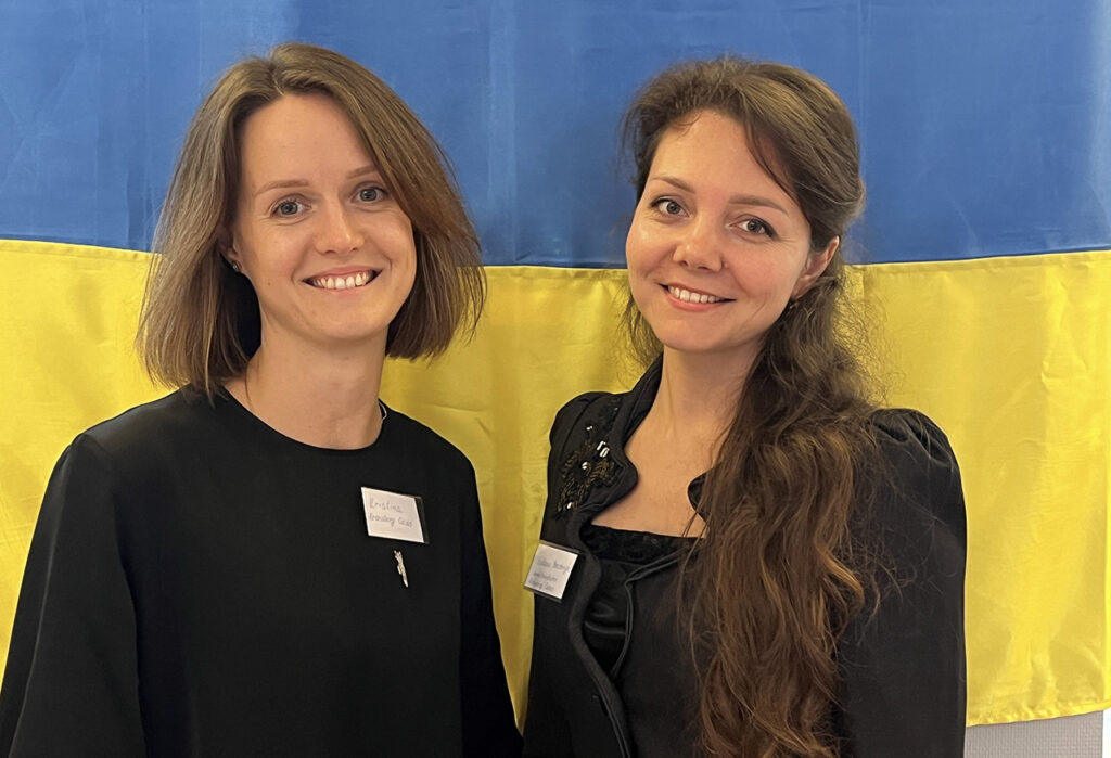 Två unga kvinnor framför en ukrainsk flagga ler mot kameran.