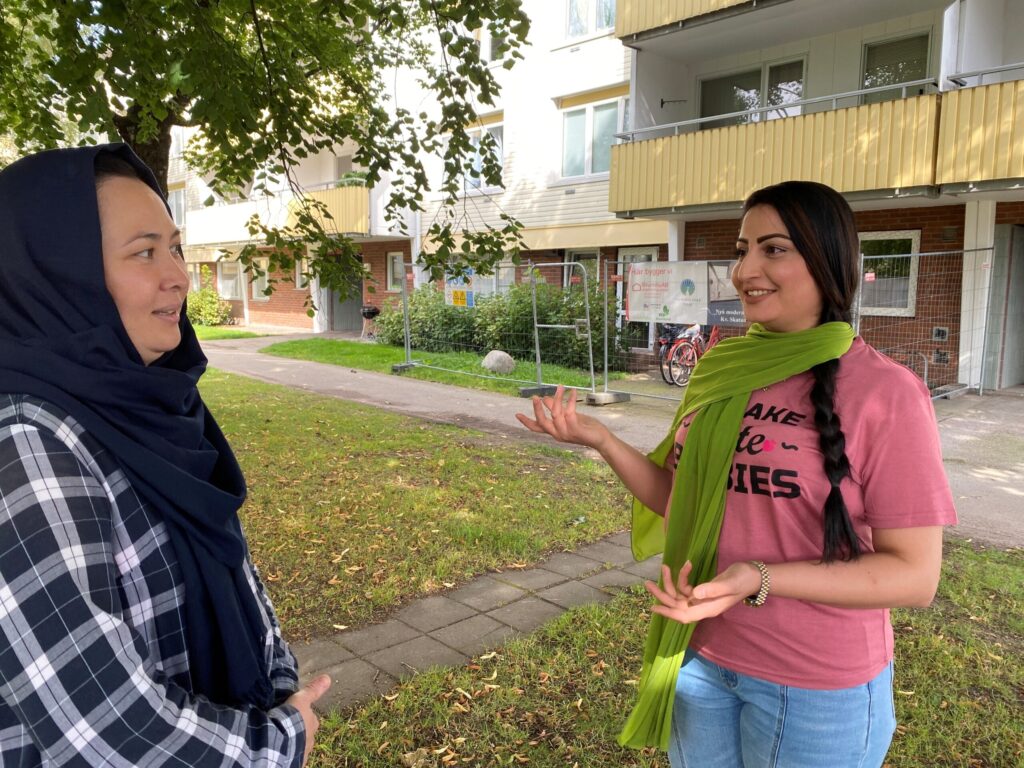 Två kvinnor talar med varandra i ett bostadsområde.