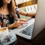Kvinna sitter vid en laptop med kaffekopp bredvid sig.