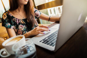 Kvinna sitter vid en laptop med kaffekopp bredvid sig.