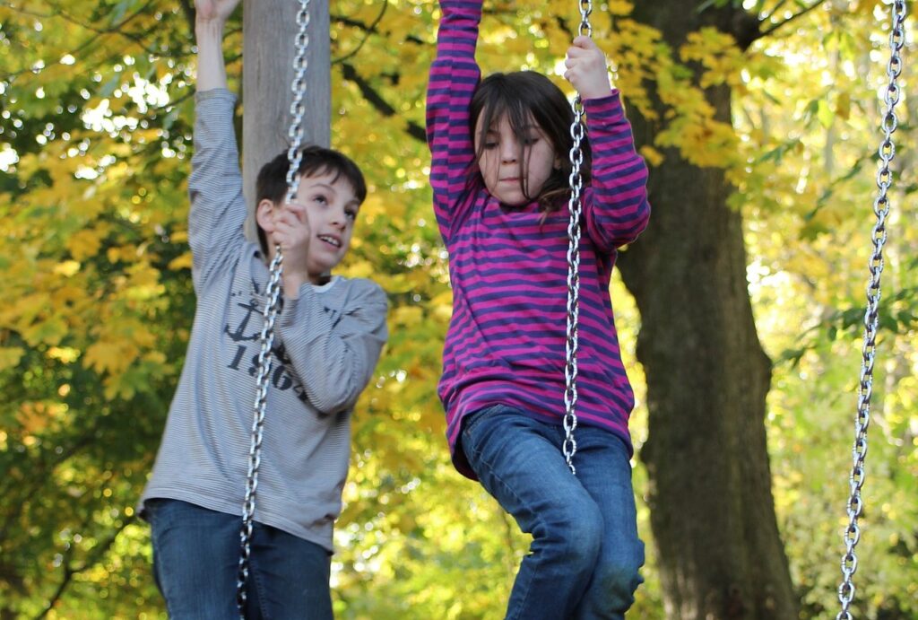 Två barn leker, hänger i kedjor på gunga.