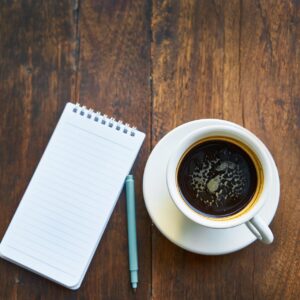 Anteckningsblock och penna bredvid kaffekopp.
