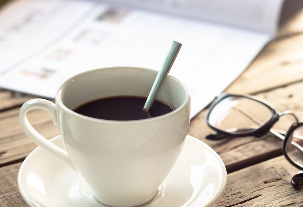 En kopp kaffe, en tidning och ett par glasögon på ett träbord.