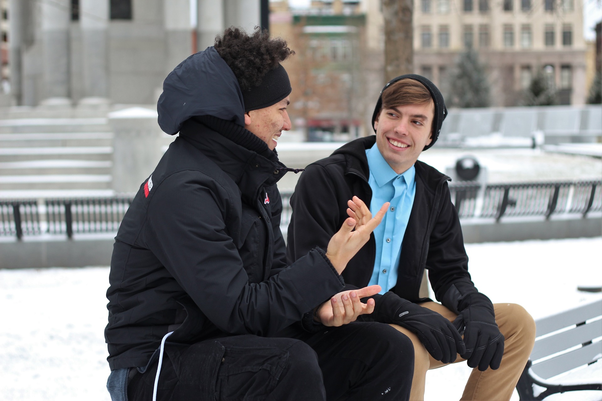 Två män sitter på en parkbänk och pratar med varandra.